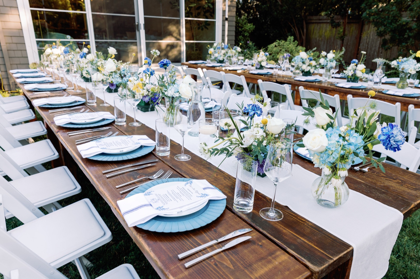 Long bar mitzvah dinner table with blue and yellow florals, blue runner, and gold flatware