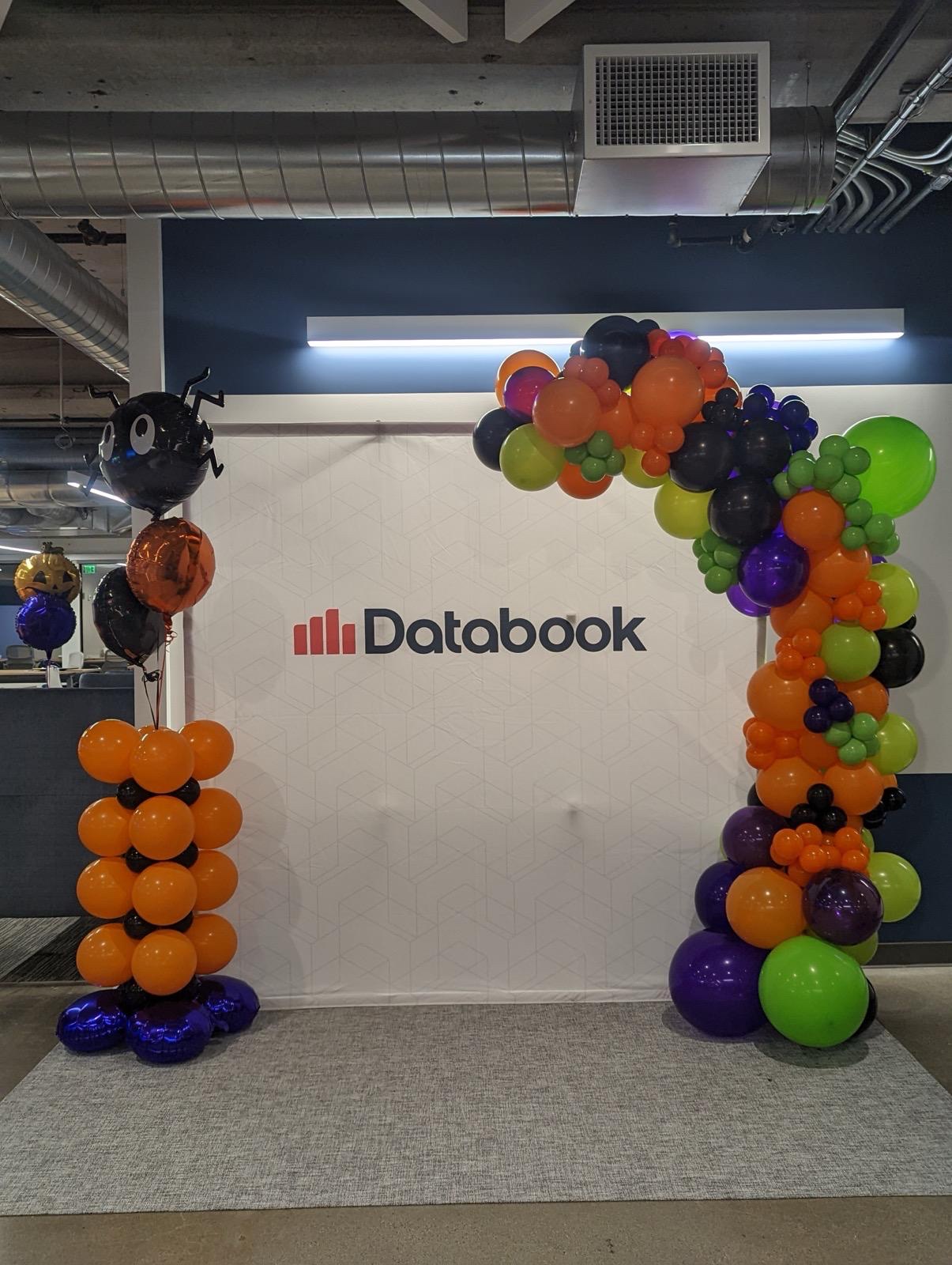 Halloween balloon arch in orange, purple, green, and black framing a Databook logo wall