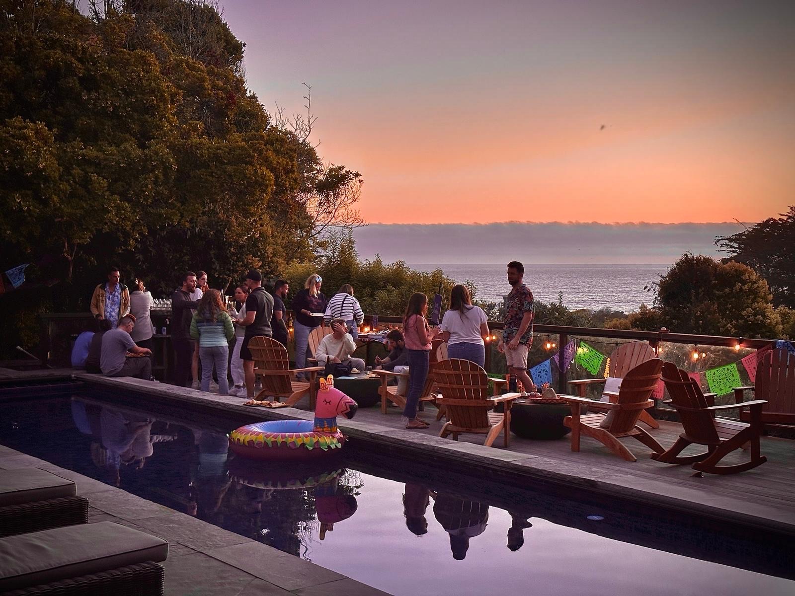 Team mixer at sunset around a pool with papel picado strung across, ocean view in the background
