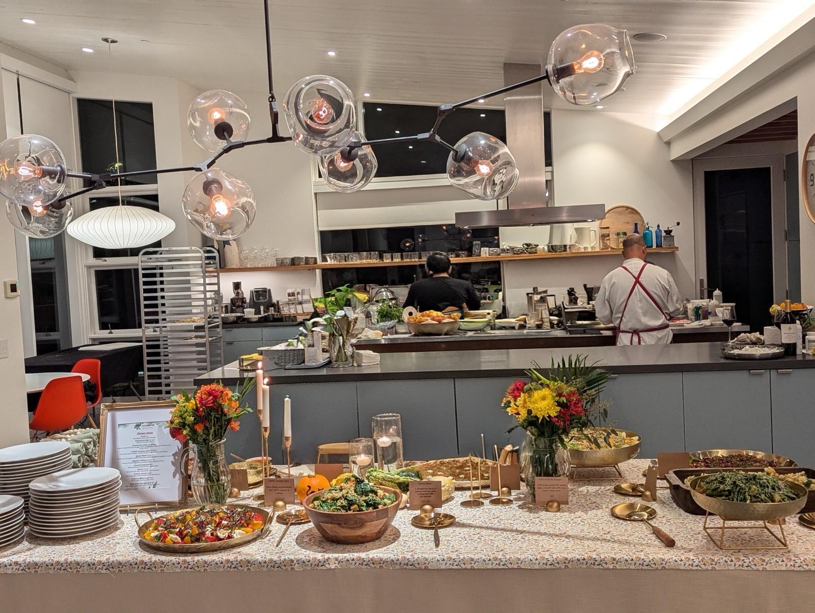 Indoor dinner party with chefs working in an open kitchen and a buffet of family-style dishes