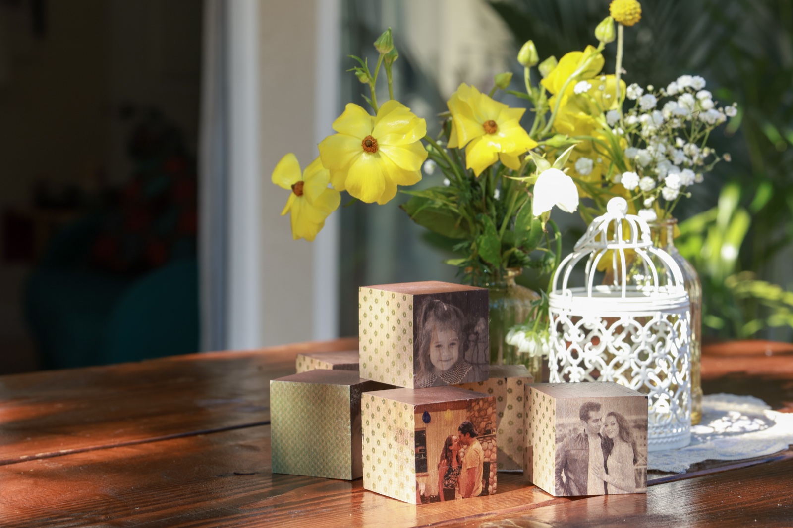 Family photo cubes and a small white birdcage on a wood table with yellow flowers