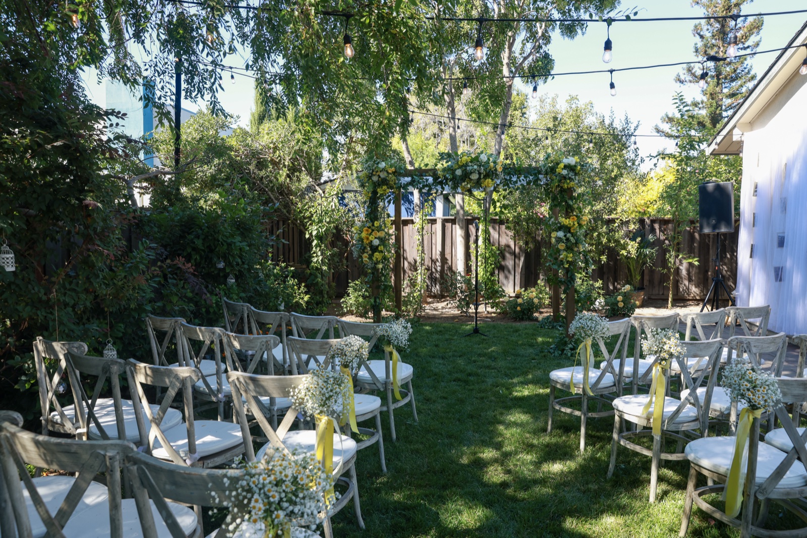 Backyard wedding ceremony with floral arch and chairs lined with baby's breath