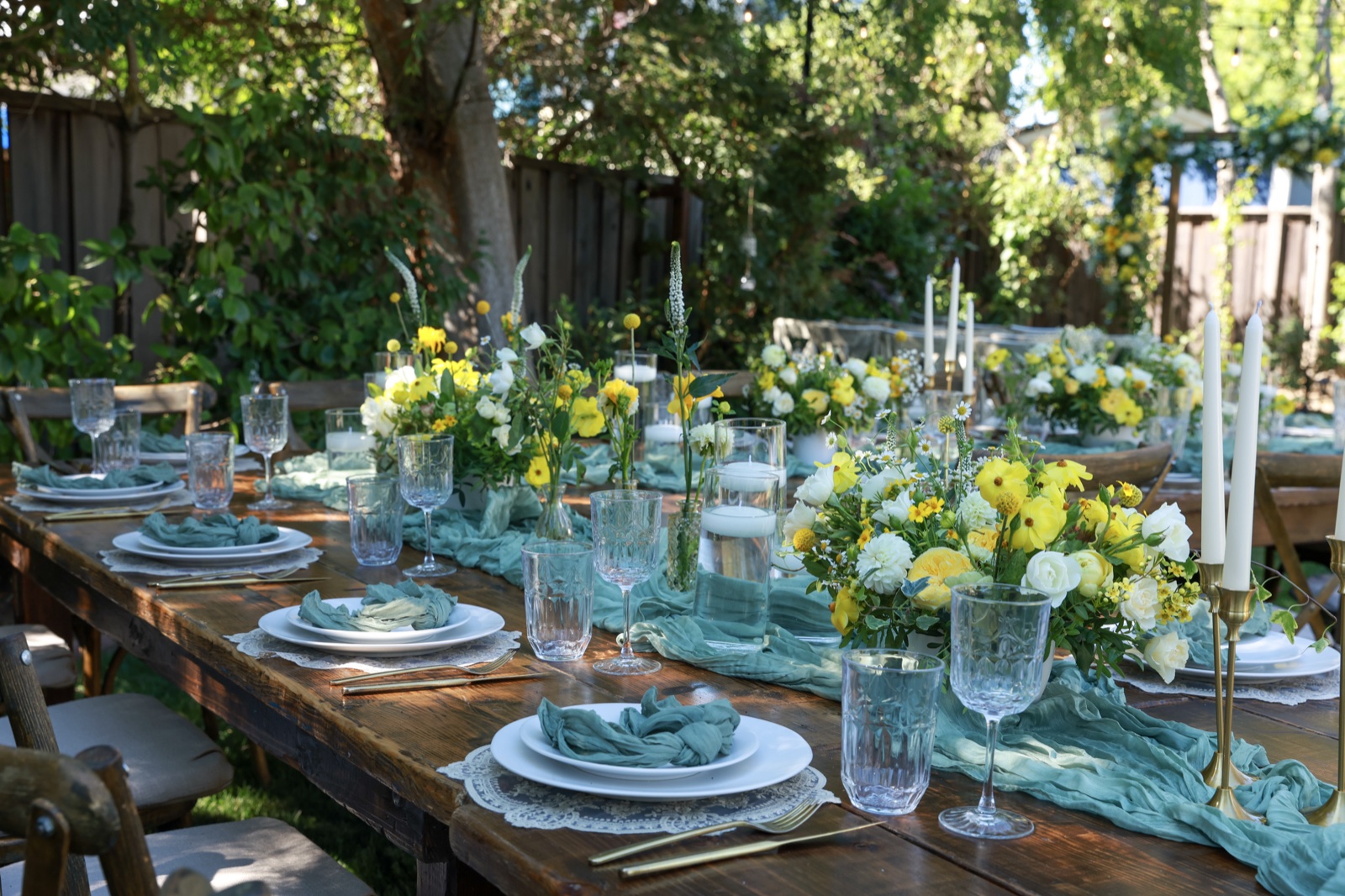 Long outdoor table set with blue, yellow, and white florals and sage chiffon runner